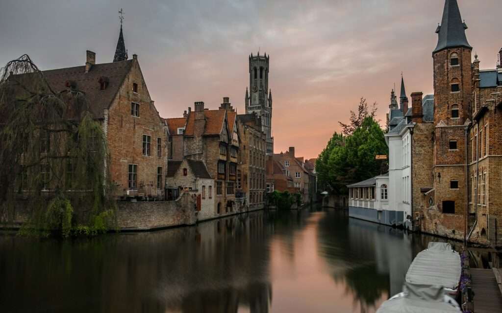The Rozenhoedkaai canal at dusk with the Belfry of Bruges behind the gabled houses